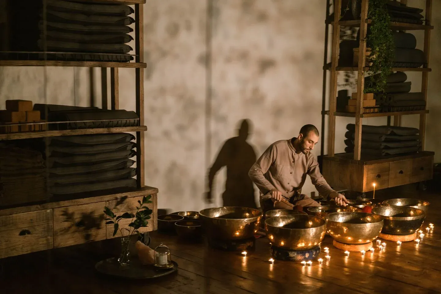Singing bowls ringed with candles on a wooden floor in a warm, low-lit room.